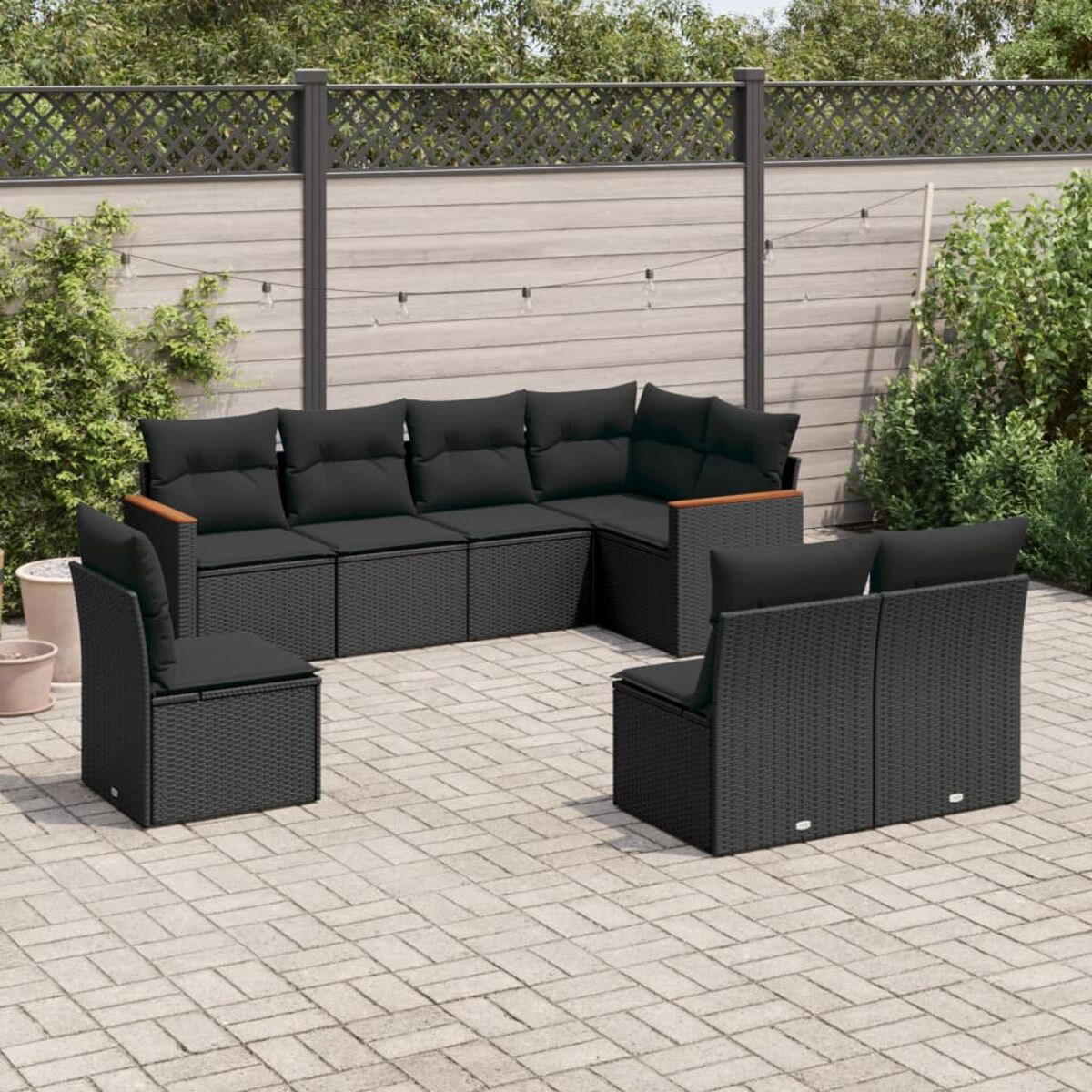 Gartenmöbel-Set. Schwarzes Ecksofa aus Korbgeflecht, Stühle und eine Backstein-Terrasse vor einem Holzzaun.