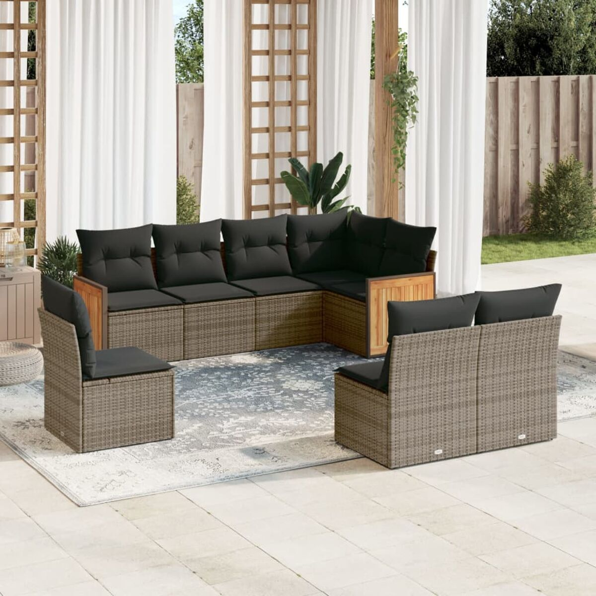 Rattan-Gartenmöbelset mit schwarzen Kissen. Set steht auf einem Teppich. Hintergrund: Vorhänge und Pflanzen.