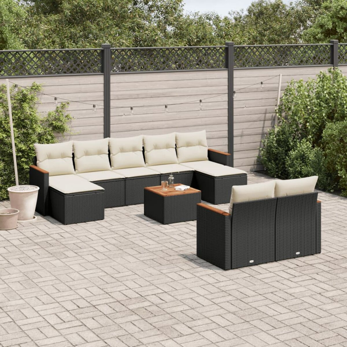 Schwarzes Korbmöbel-Set mit cremefarbenen Kissen auf einer Ziegelterrasse.