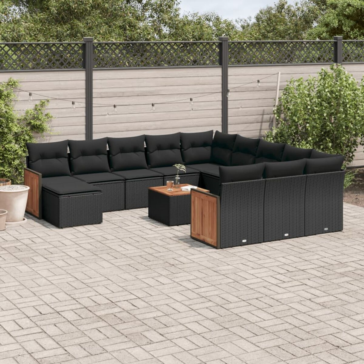 Schwarzes Wicker-Outdoor-Sofa. Inklusive Holztisch. Ziegelterrasse, Zaun und Pflanzen.