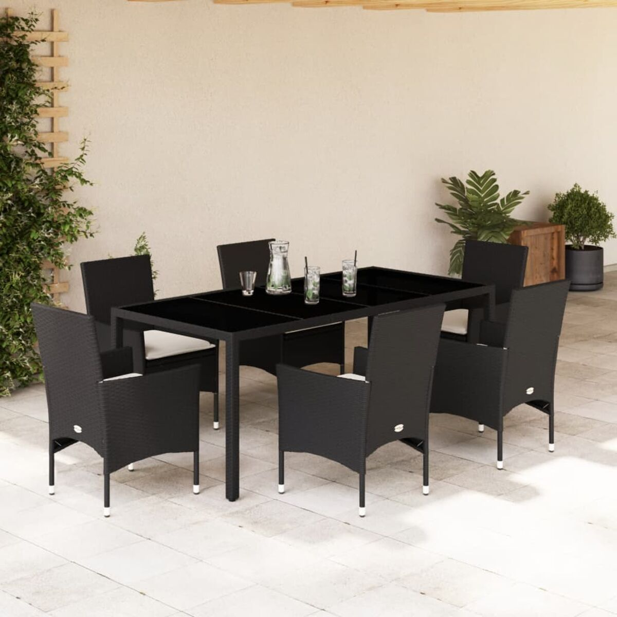 Schwarzer Esstisch aus Korbgeflecht und sechs Stühle mit schwarzen Kissen. Gläser, Pflanzen und heller Hintergrund.