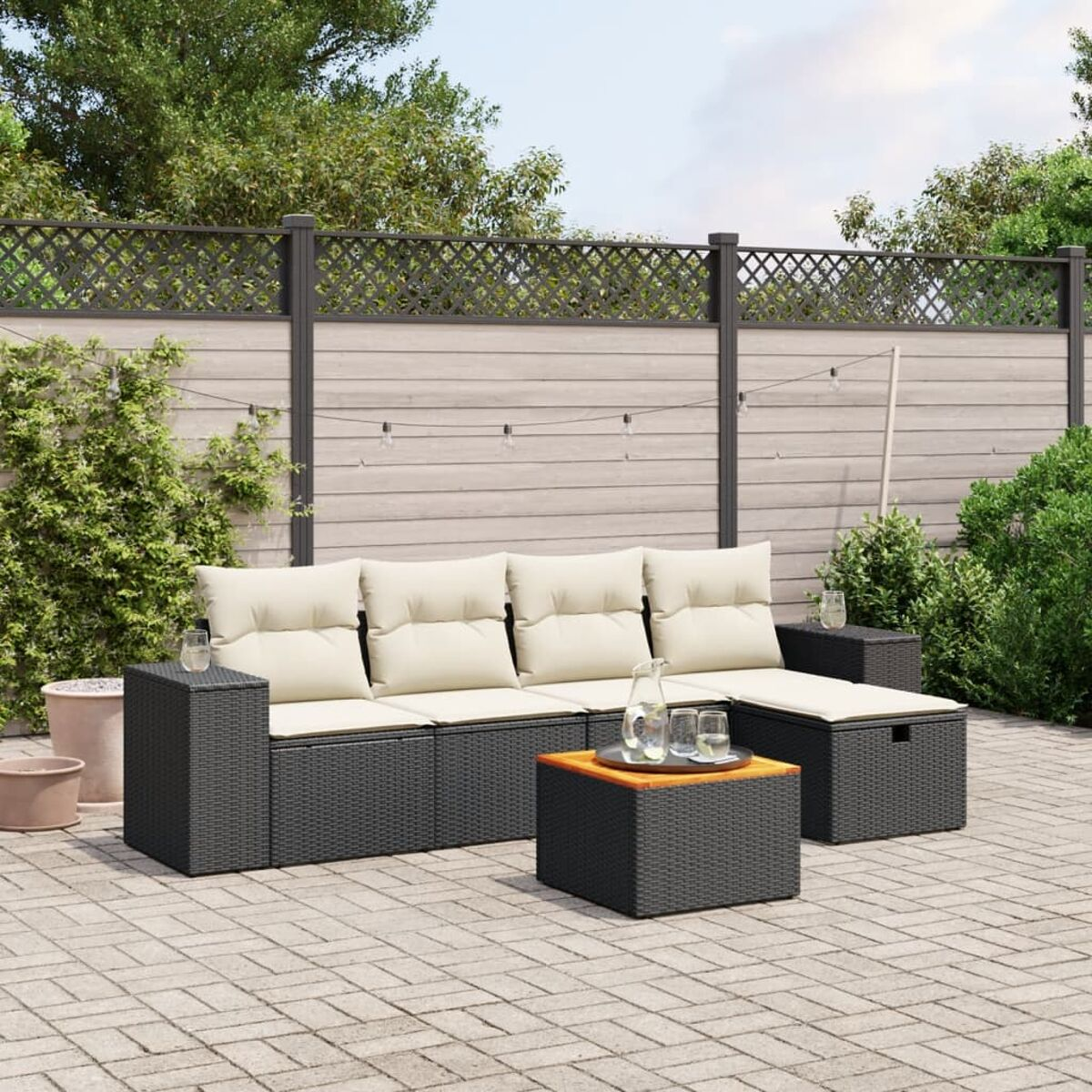 Terrassenset im Freien. Dunkelgraues Korbmöbel-Sofa mit cremefarbenen Kissen, Couchtisch.