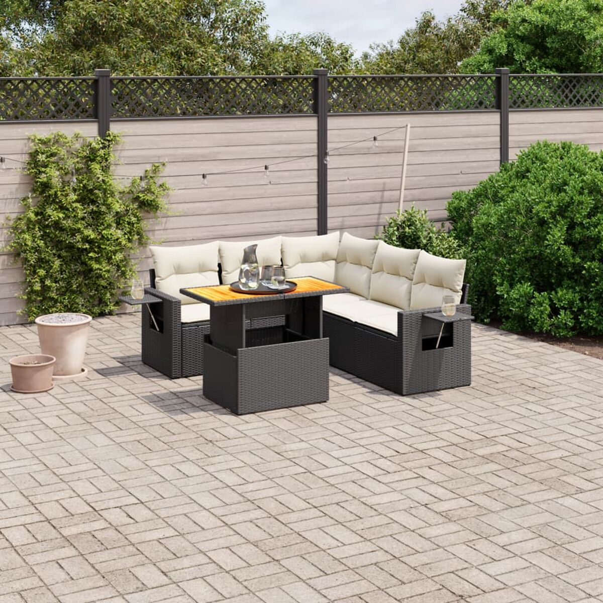 Terrassen-Set mit Korbmöbeln, Tisch und Kissen. Ziegel-Patio, Zaun und Pflanzen.