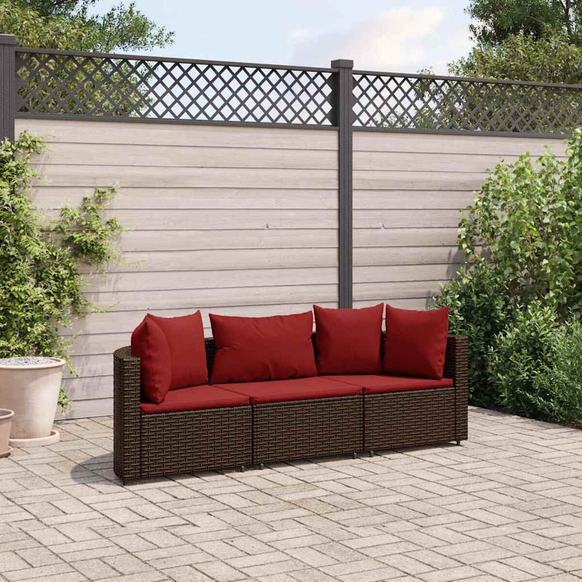 Divano in rattan marrone con cuscini rossi su un patio in mattoni.