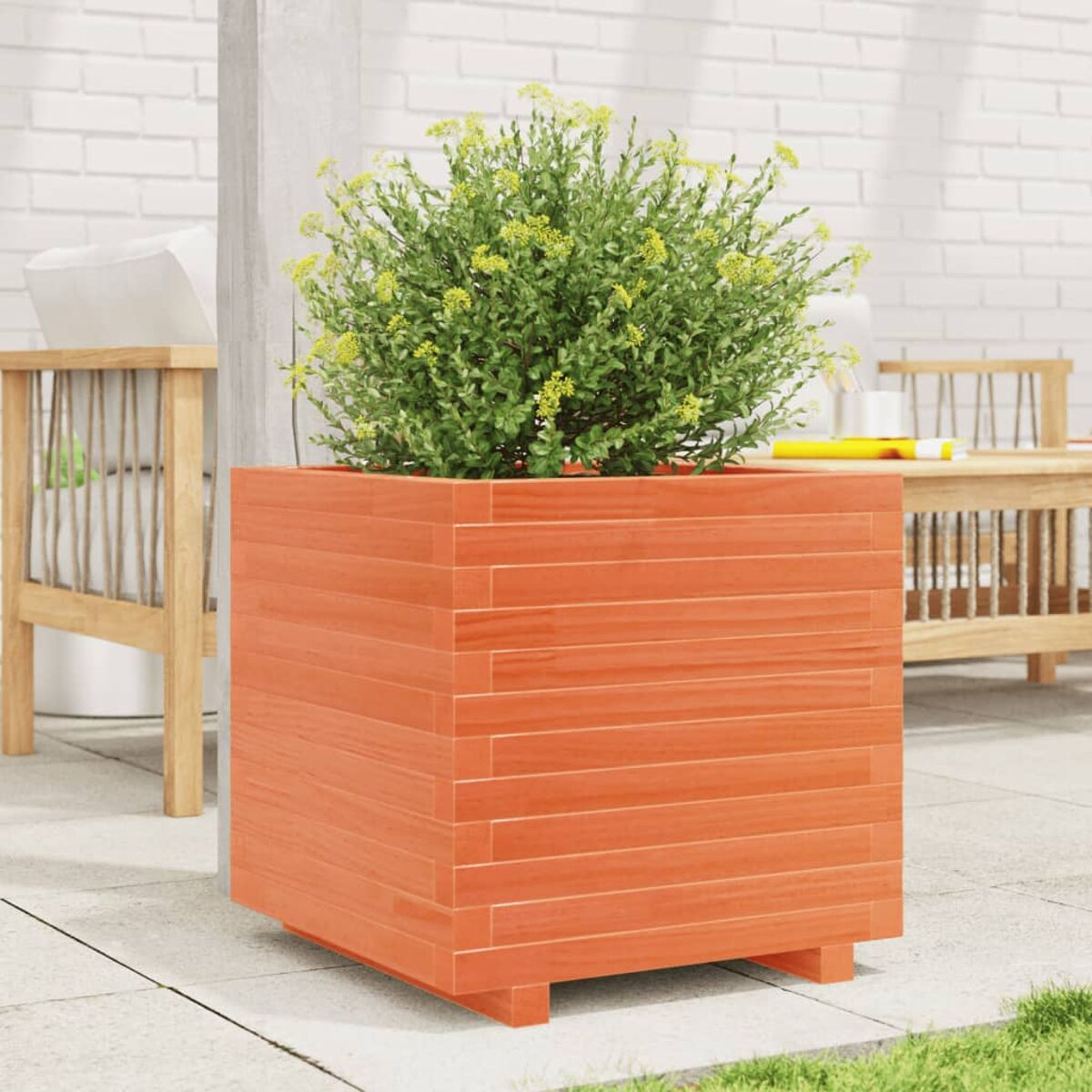 Orangener Holzpflanzkübel mit grüner Pflanze. Im Hintergrund eine Terrasse mit Möbeln.
