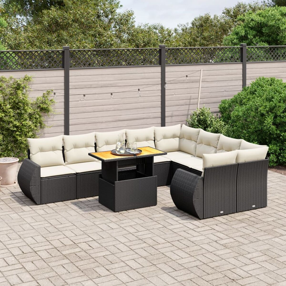 Outdoor-Ecksofa mit beigen Kissen, schwarzem Tisch. Szene enthält Zaun, Grün und Backstein-Patio.
