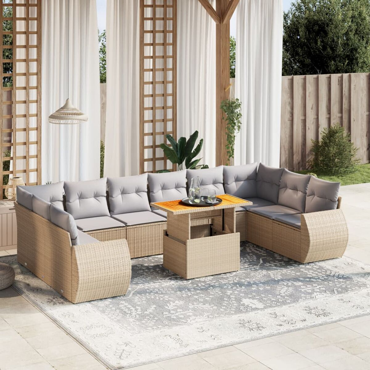 Outdoor-Korbmöbel-Set mit hellgrauen Kissen. Beinhaltet einen Tisch und einen Teppich. Der Hintergrund hat Vorhänge und ein Spalier.