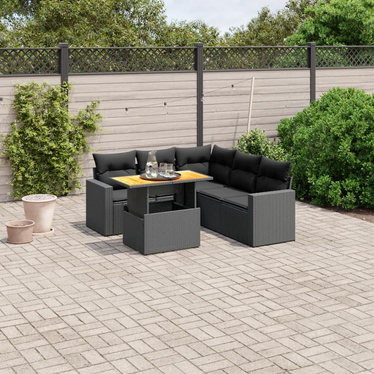 Terrassenmöbel-Set mit grauen Korbmöbeln und schwarzen Kissen. Inklusive Tisch und Topfpflanzen.