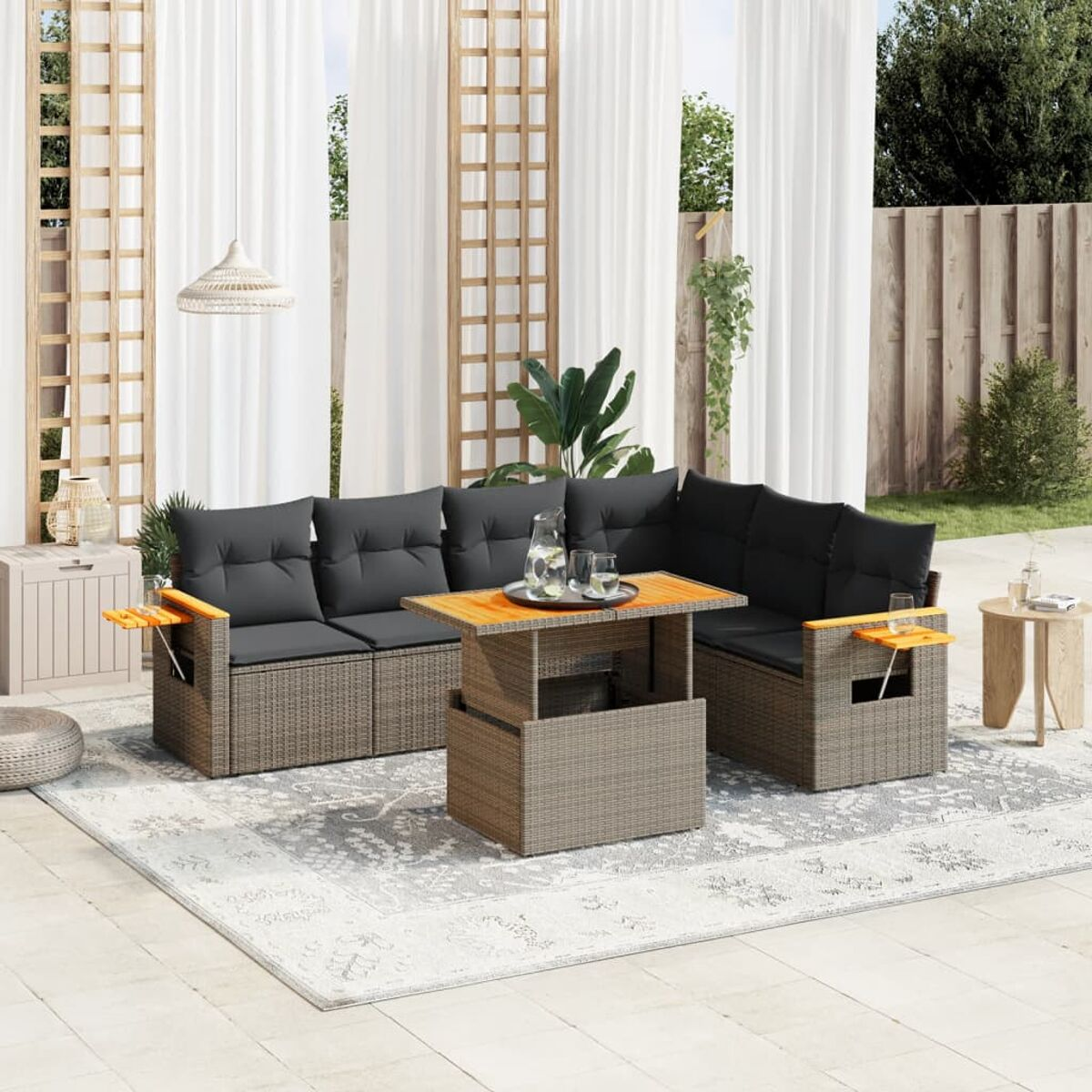 Ein Rattan-Sitzgruppe mit grauen Kissen und einem Tisch mit Hubplatte. Weiße Vorhänge und Teppich sind im Bild.