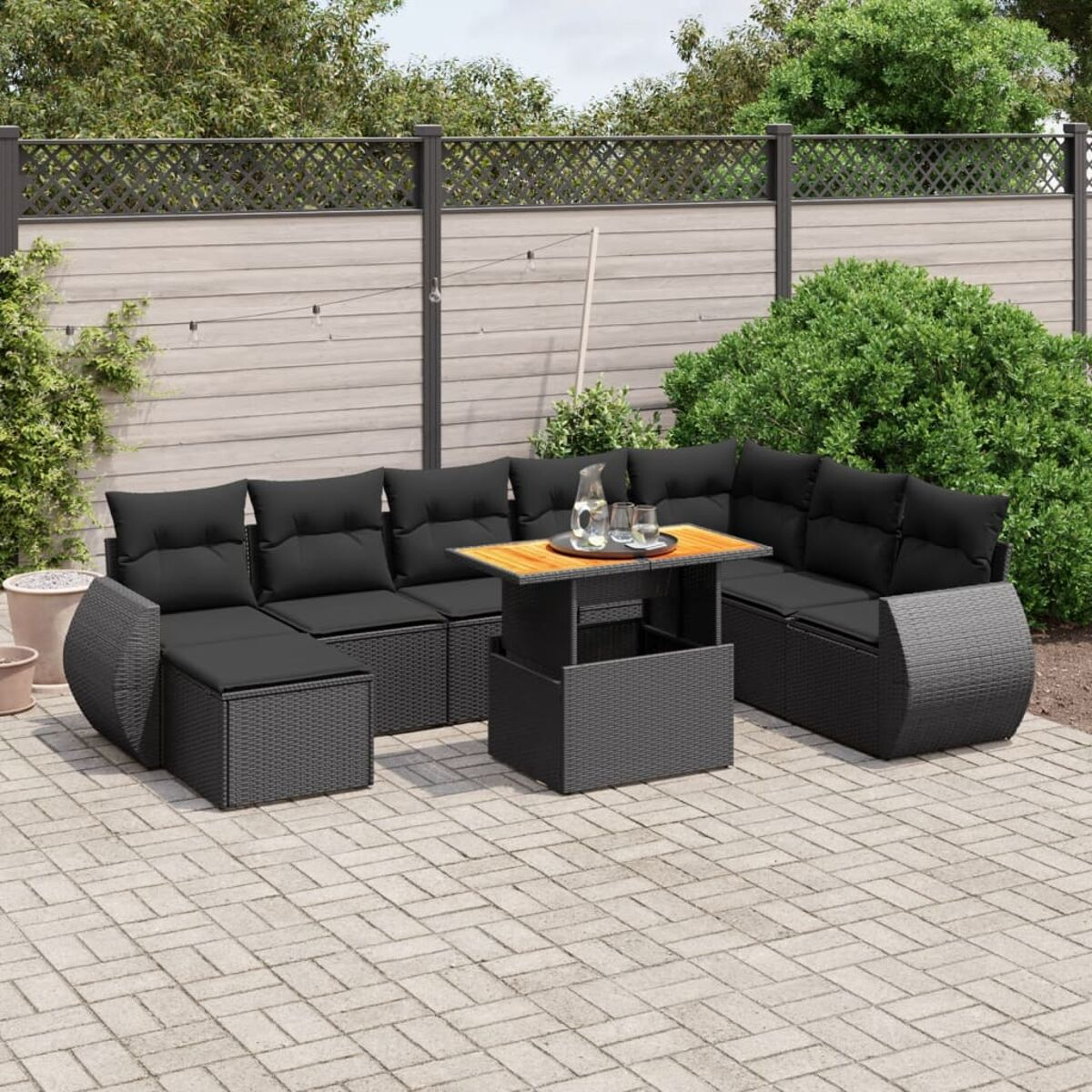 Outdoor-Sofa mit schwarzen Kissen, Tisch und Blick in den Garten mit Grün.