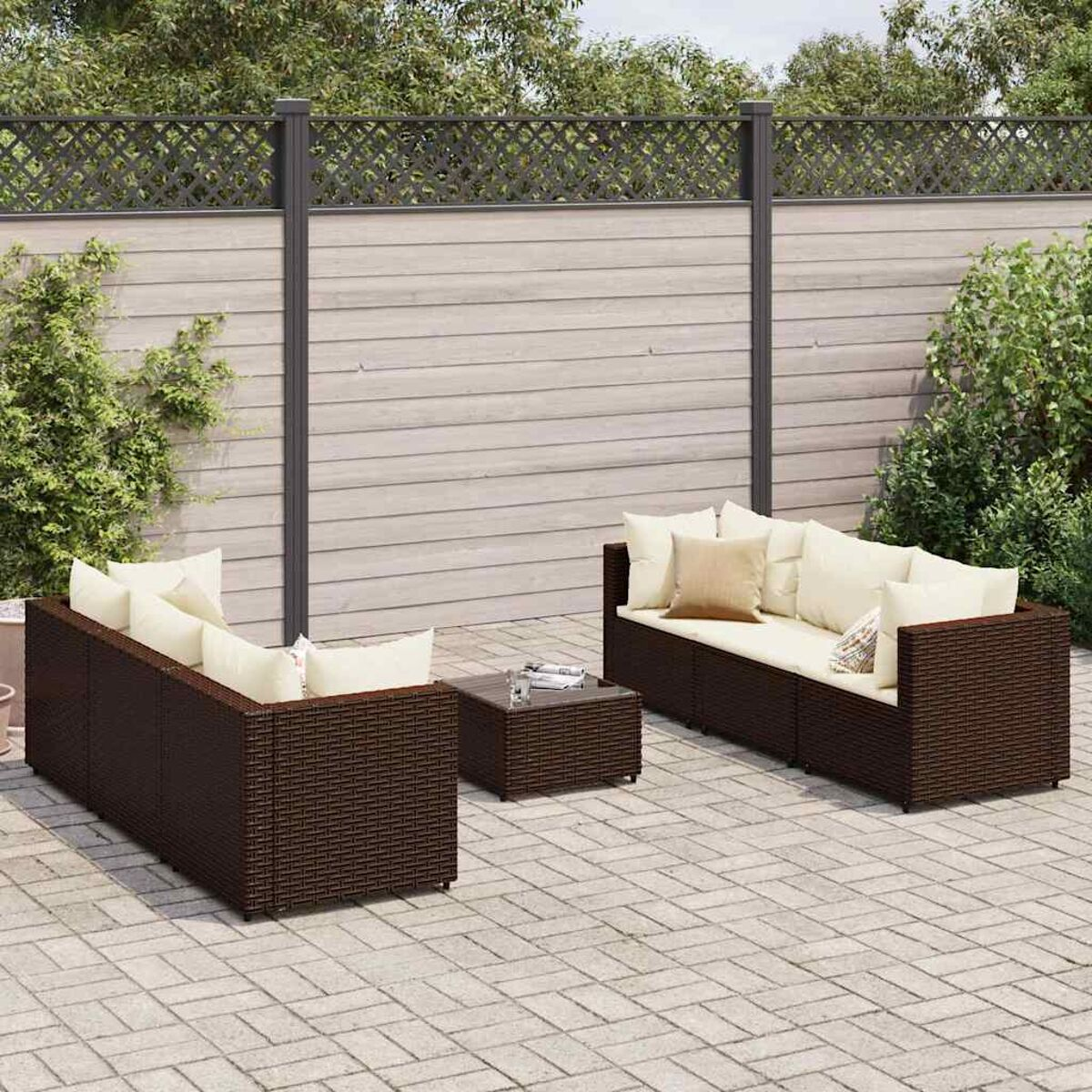Set di divani da esterno in vimini marrone con cuscini color crema e un tavolino. Il set è su un patio in mattoni.