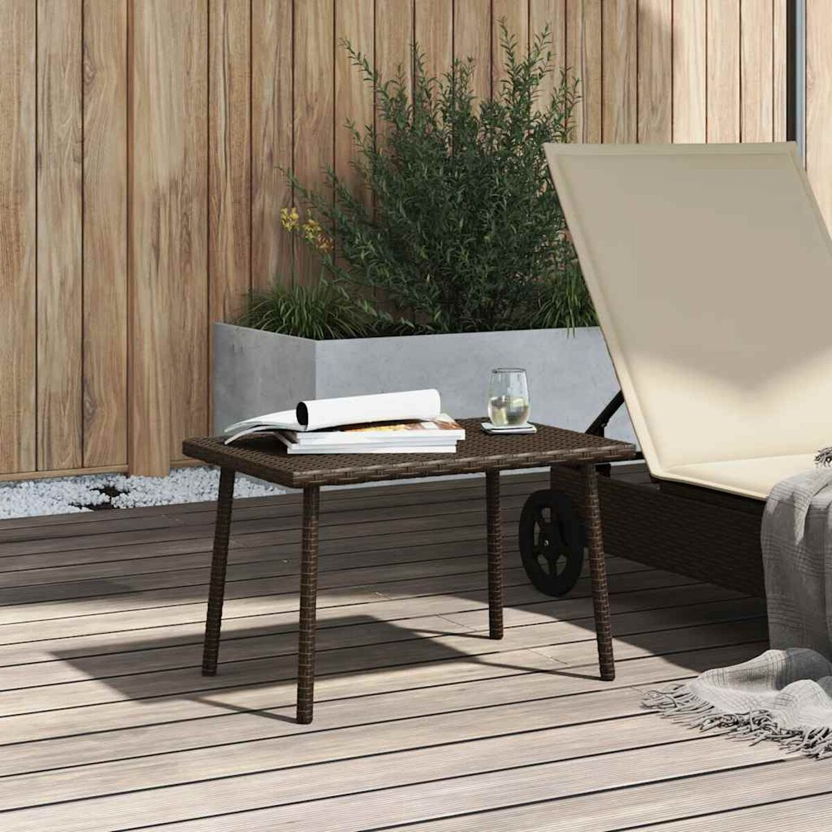 Kleiner brauner Korbtisch mit Büchern, Glas und Pflanze auf einem Holzdeck.