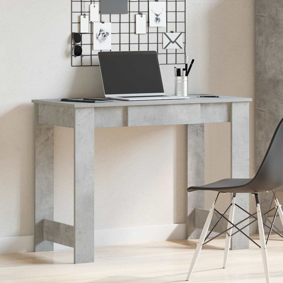 Ein grauer Schreibtisch mit Laptop, Notizbuch, Stift und schwarzem Gitter an einer weißen Wand.