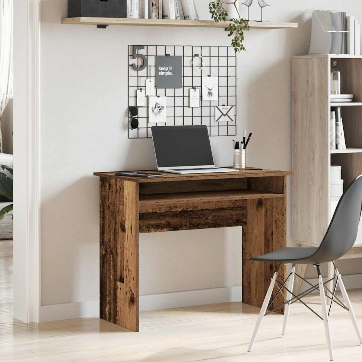 Holzschreibtisch mit Laptop, Zubehör und schwarzem Stuhl. Ein Drahtgitter mit Notizen an der Wand.
