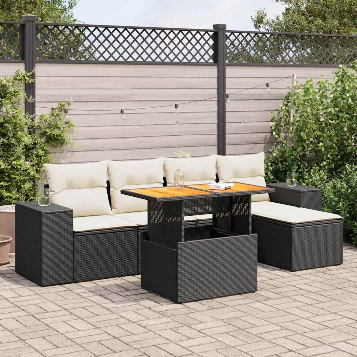 Divano componibile nero da esterno con tavolo sollevabile, su un patio pavimentato con piante.