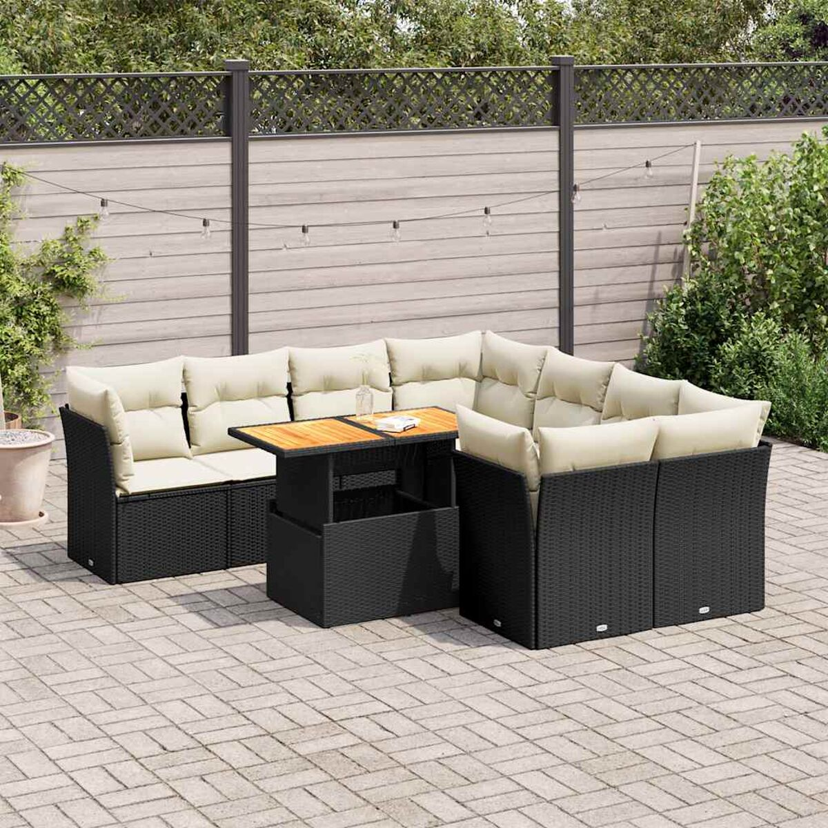 Divano angolare in rattan nero con cuscini beige e tavolo su un patio pavimentato.
