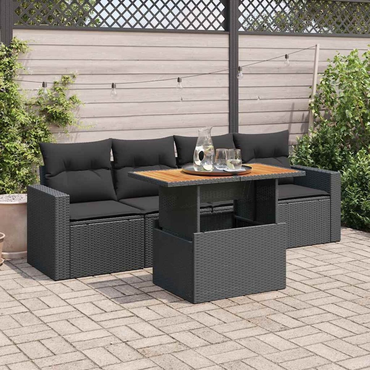 Set di sedute da esterno con cuscini neri e tavolino con piano in legno.