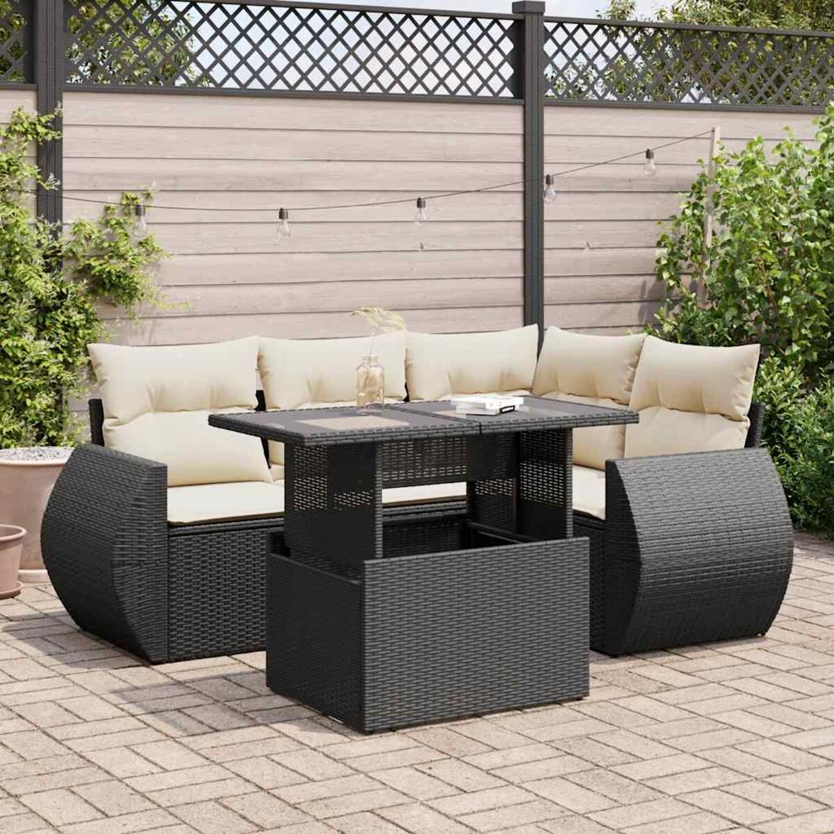 Set da patio in rattan nero con cuscini beige. Un tavolo al centro, su pavimento in mattoni.