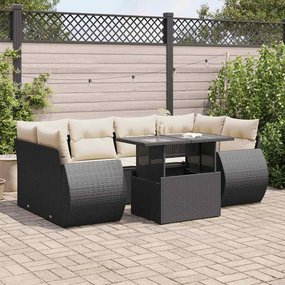 Set patio in rattan scuro con tavolo e divano. Lo sfondo ha una recinzione e vegetazione.
