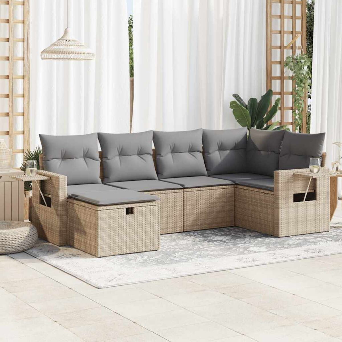 Set divano in rattan da esterno con cuscini, tavolini e tappeto fantasia.