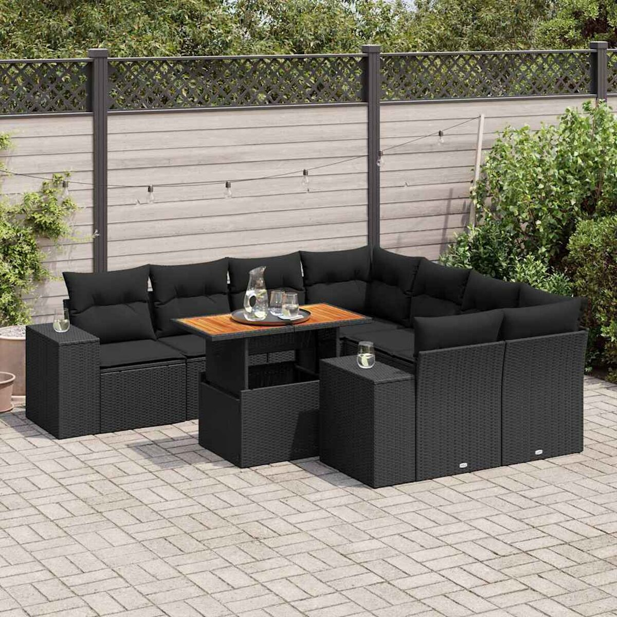 Schwarzes Outdoor-Ecksofa aus Korbgeflecht mit Kissen, Holztisch und Beistelltischen. Auf einer Backstein-Terrasse.