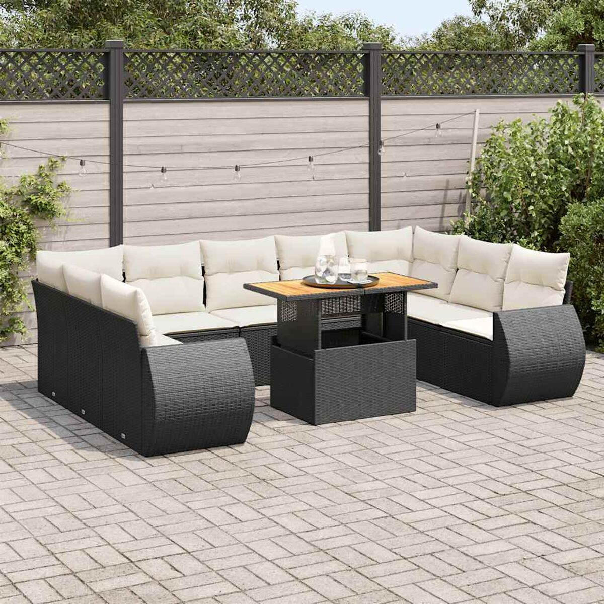 Set divano componibile da esterno, nero. Tavolo con bevande. Patio, recinzione, cespugli.