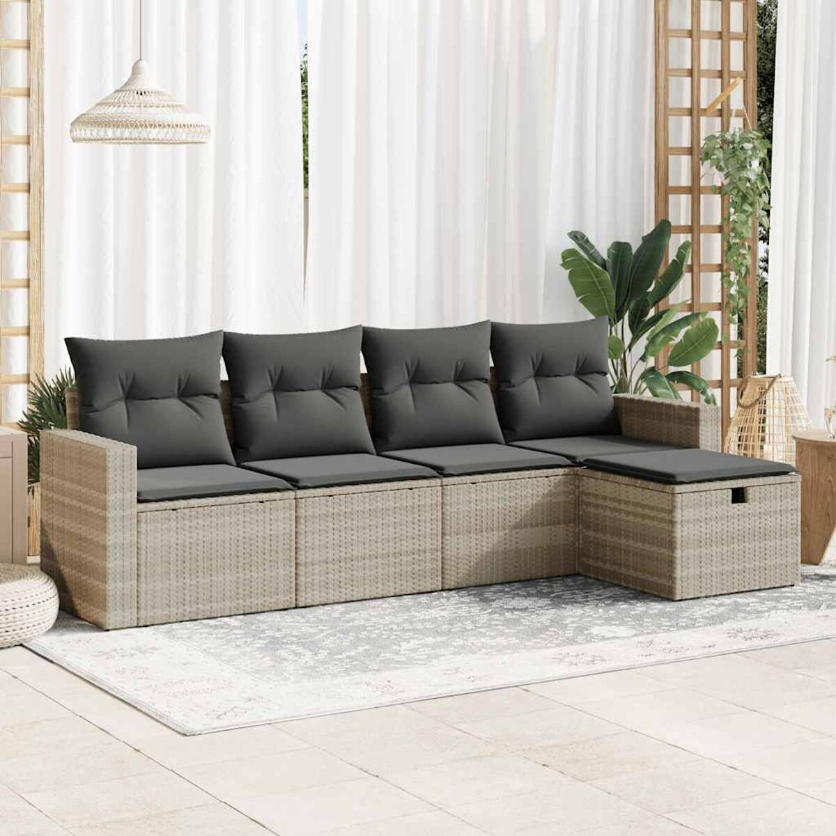Geflochtenes Modulsofa mit Kissen. Ein Teppich und Pflanzen sind sichtbar. Hintergrund ist weiß.