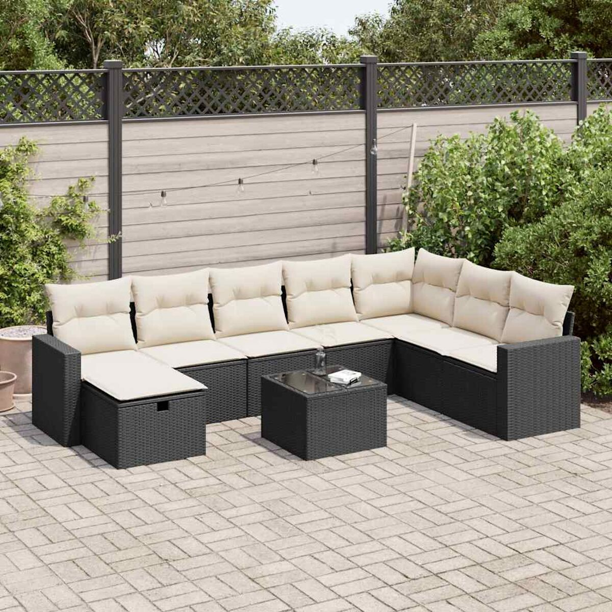 Outdoor-Sitzgruppe mit dunklen Kissen auf einer Terrasse. Enthält einen Couchtisch und Grün.