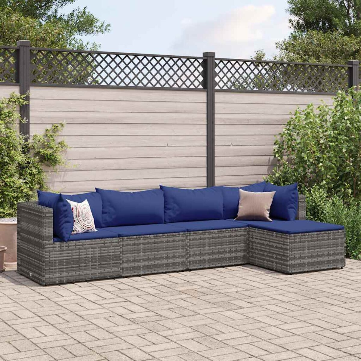 Graues Outdoor-Ecksofa, blaue Kissen. Ziegelterrasse, neutraler Zaun, sonniger Tag.