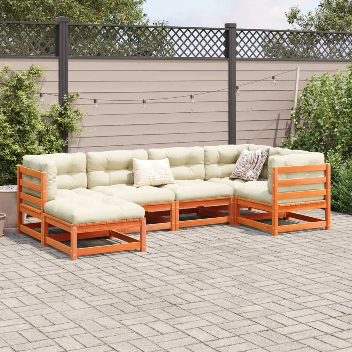 Outdoor-Ecksofa mit beigen Kissen, Holzrahmen, auf einer gepflasterten Terrasse. Im Hintergrund ein Zaun und Grün.