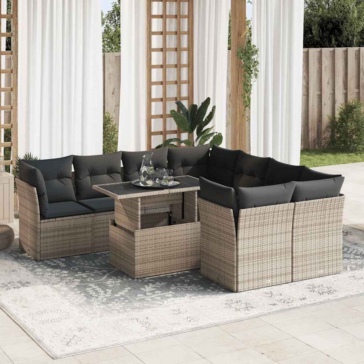 Set di mobili da esterno in rattan con tavolo e sedute. Cuscini neri, struttura marrone chiaro.