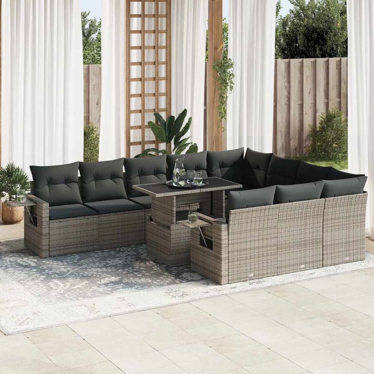 Divano componibile in rattan grigio con cuscini neri, un tavolo e bicchieri. Ambiente esterno.