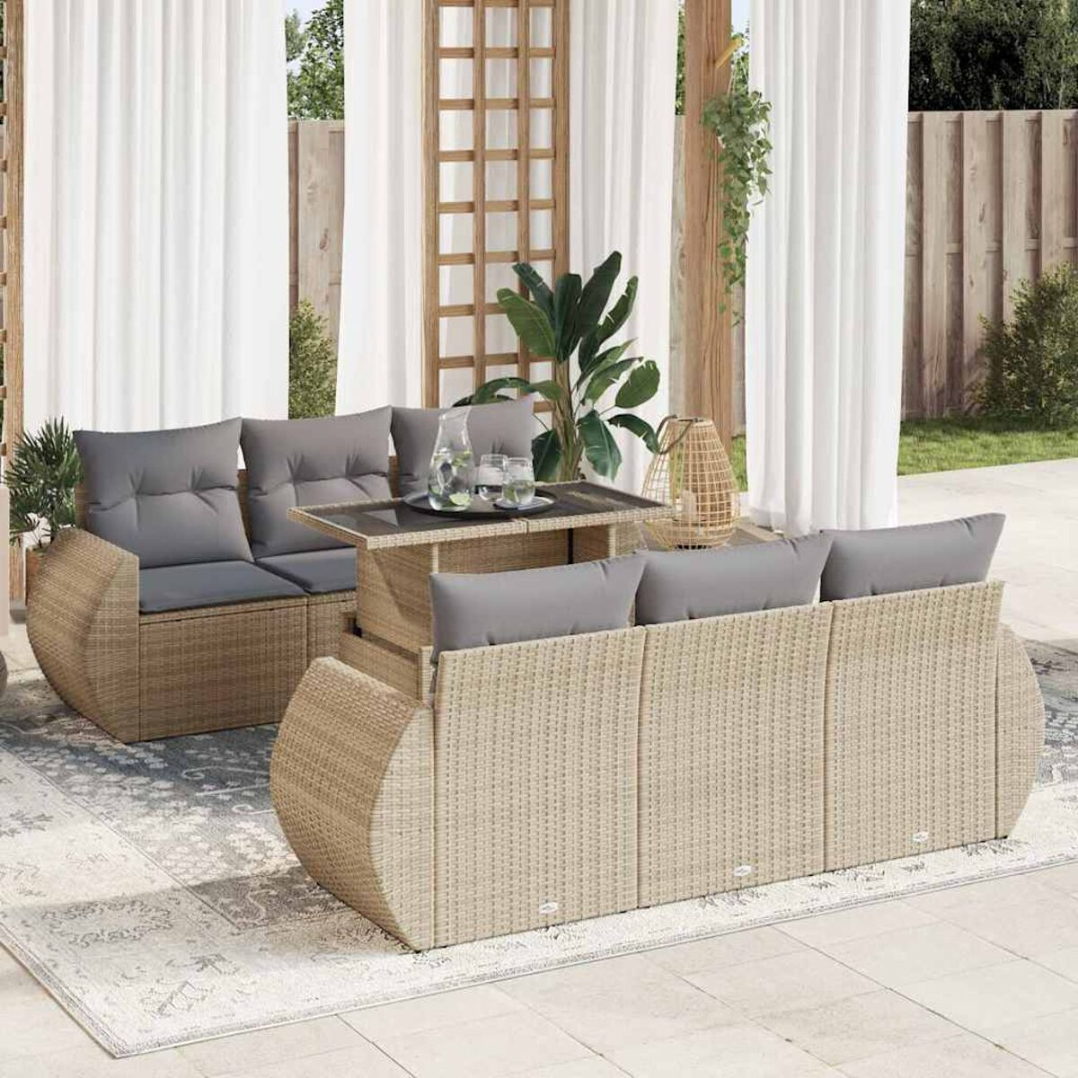 Geflochtenes Terrassenset mit Tisch und Sofa, mit Vorhängen und einem Baum im Hintergrund.