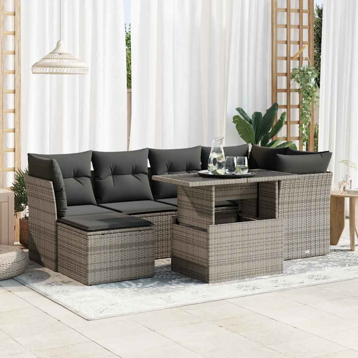 Set di sedute per esterni con cuscini grigi e design intrecciato, su un tappeto, con tende e piante.