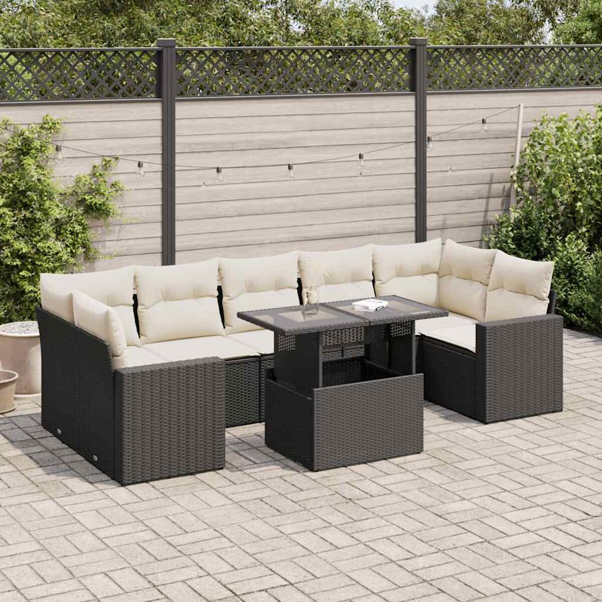 Divano componibile da esterno grigio scuro con cuscini beige e un tavolo su un patio in mattoni con una recinzione sullo sfondo.