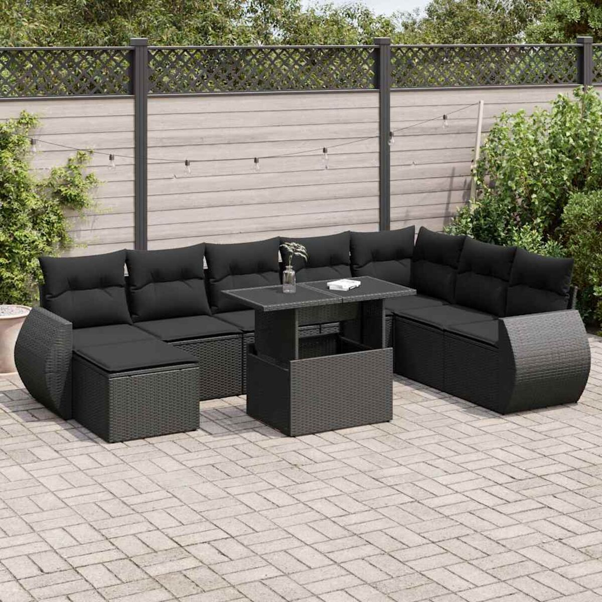 Set divano in vimini nero per esterni. Include un divano componibile e un tavolino. Patio pavimentato sullo sfondo.
