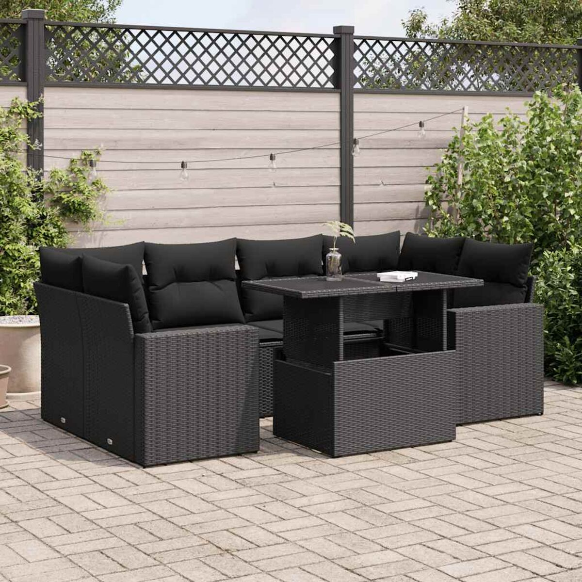 Schwarzes Outdoor-Geflecht-Sofaset mit Tisch. Schwarze Kissen. Gepflasterte Terrasse, grauer Zaun.