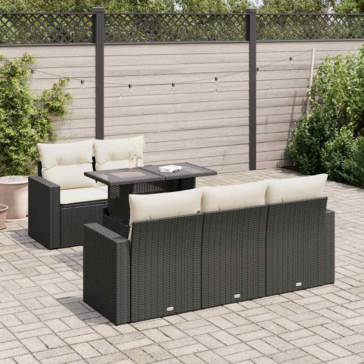 Set di mobili da esterno in vimini nero con tavolo e cuscini beige. Recinto sullo sfondo.