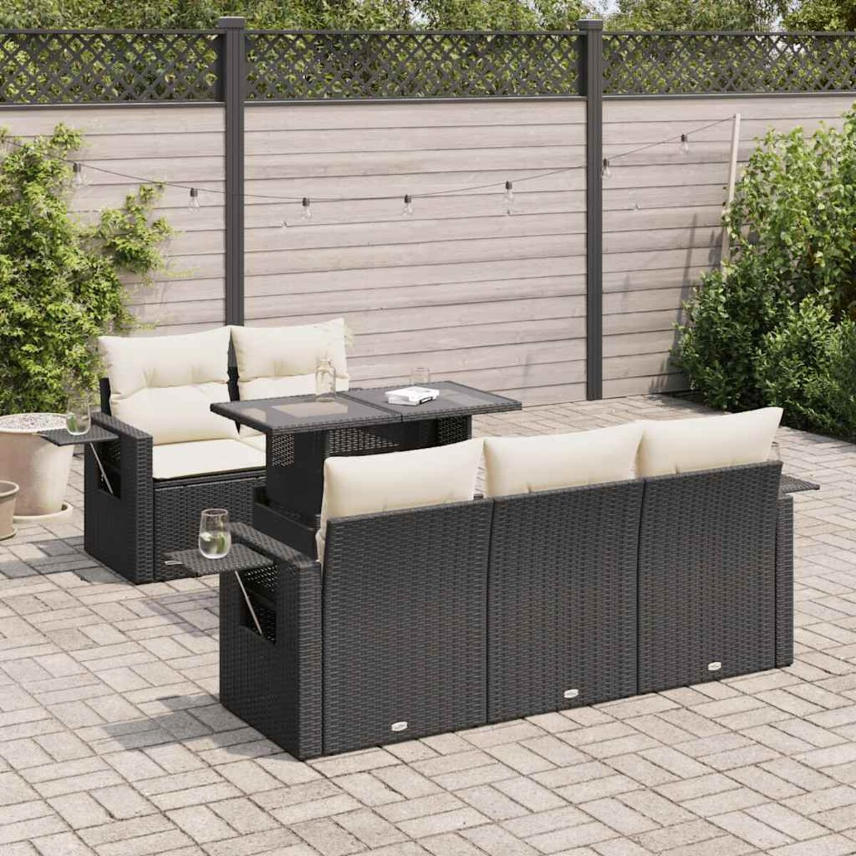 Un juego de asientos de exterior con muebles de mimbre negro, cojines blancos y una mesa con tapa de cristal.