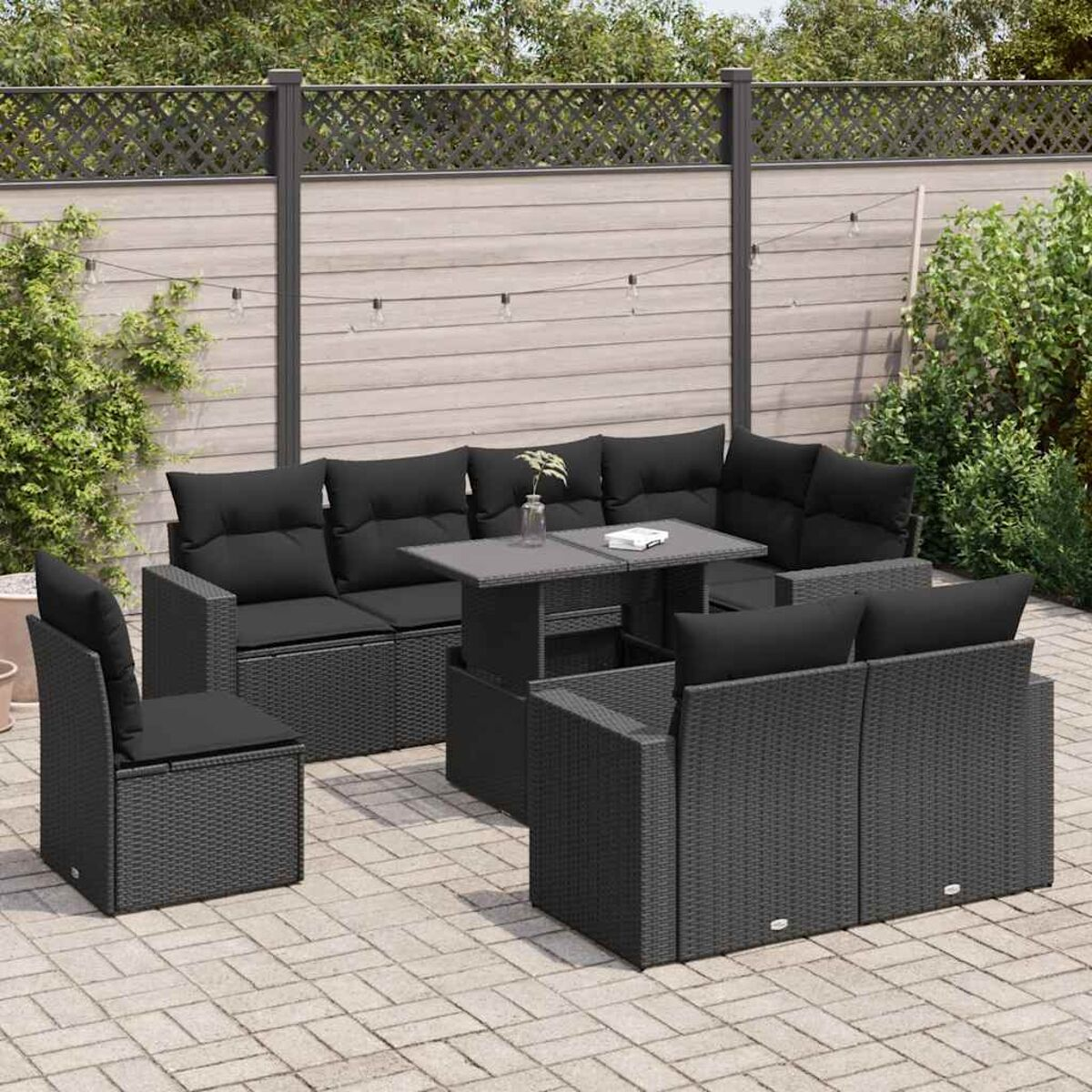 Set patio in vimini grigio scuro con tavolo, sedie e cuscini. Recinzione in legno sullo sfondo.