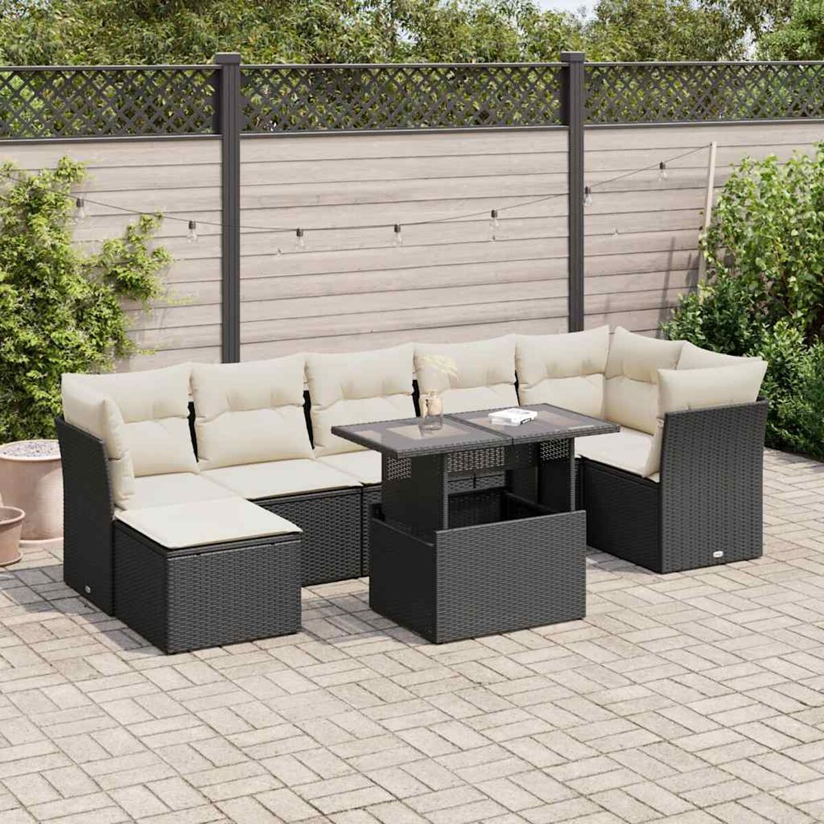 Set di mobili da esterno. Struttura nera, cuscini beige, su un patio. Tavolo al centro. Sfondo: recinzione.