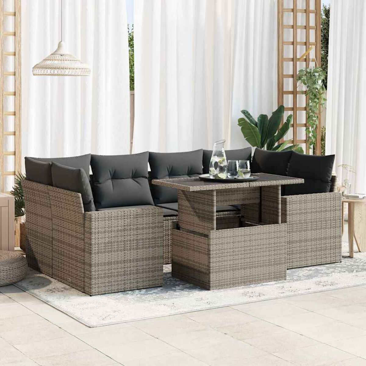 Set divani da esterno in rattan grigio con un tavolo. Include cuscini, su un patio. Tende e piante visibili.