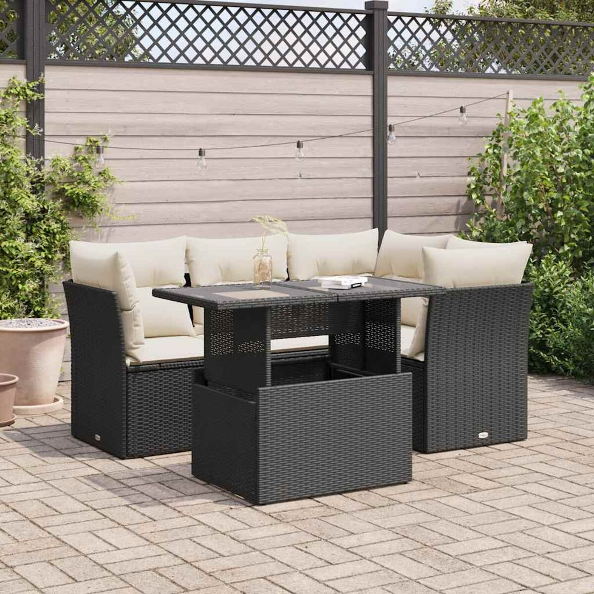 Divano angolare in rattan nero con cuscini beige e tavolo su un patio.