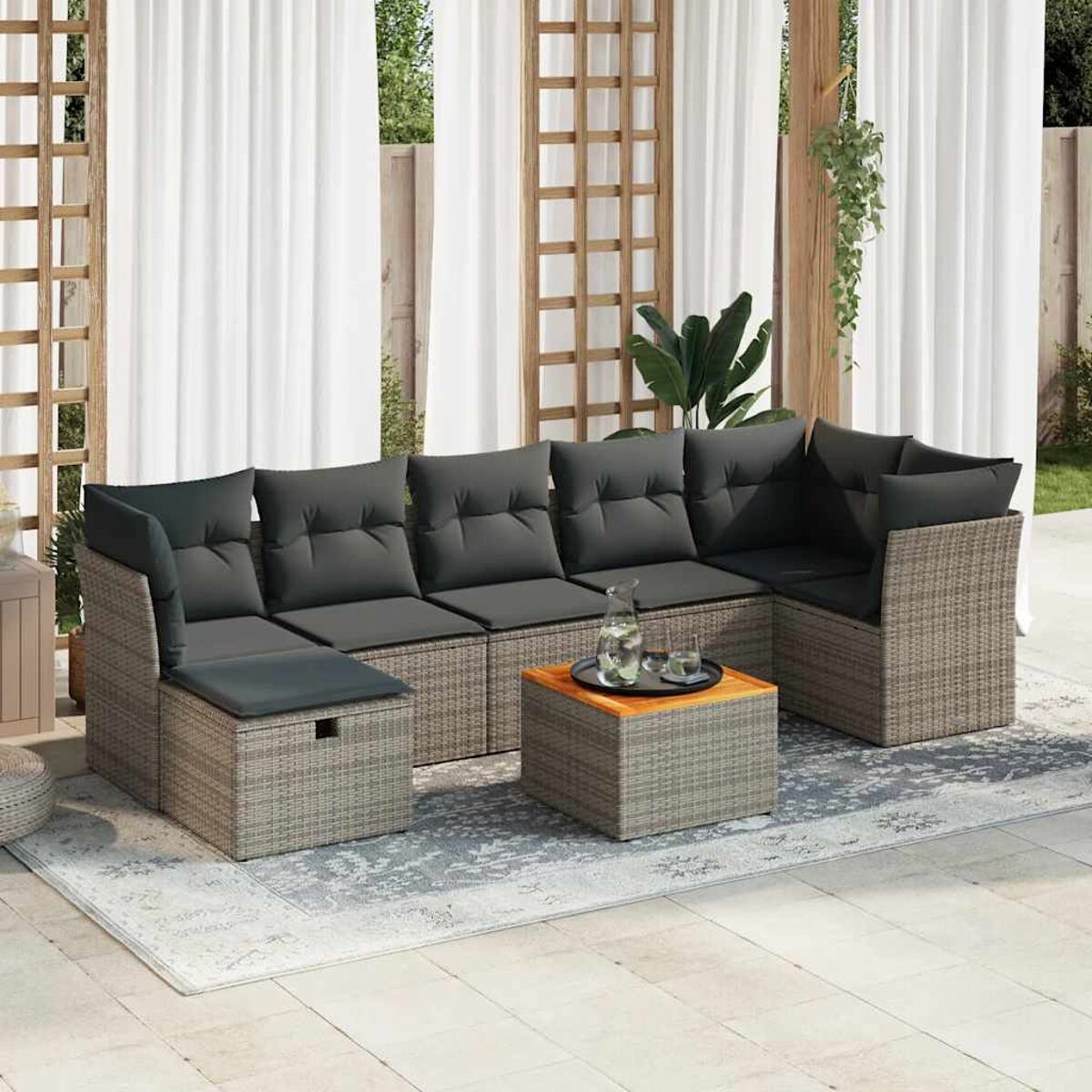 Outdoor-Ecksofa mit grauen Kissen, Weidenrahmen und Couchtisch auf einer Terrasse mit Vorhängen.