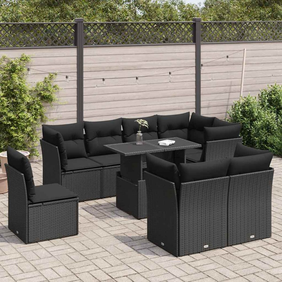 Set divani in vimini nero per esterni. Cuscini neri, tavolo. Patio in mattoni, recinzione.