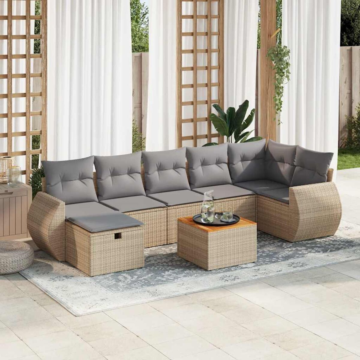 Set divano in rattan da esterno con cuscini grigi e un tavolo, vicino alle tende.