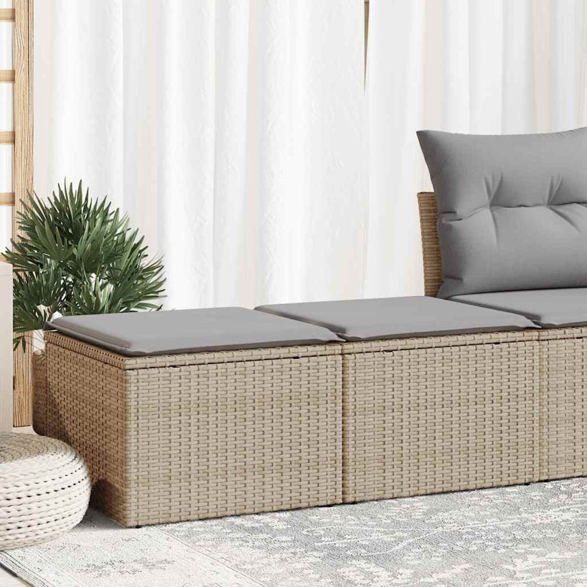 Primo piano di un divano in rattan beige con cuscini grigi su un tappeto chiaro.