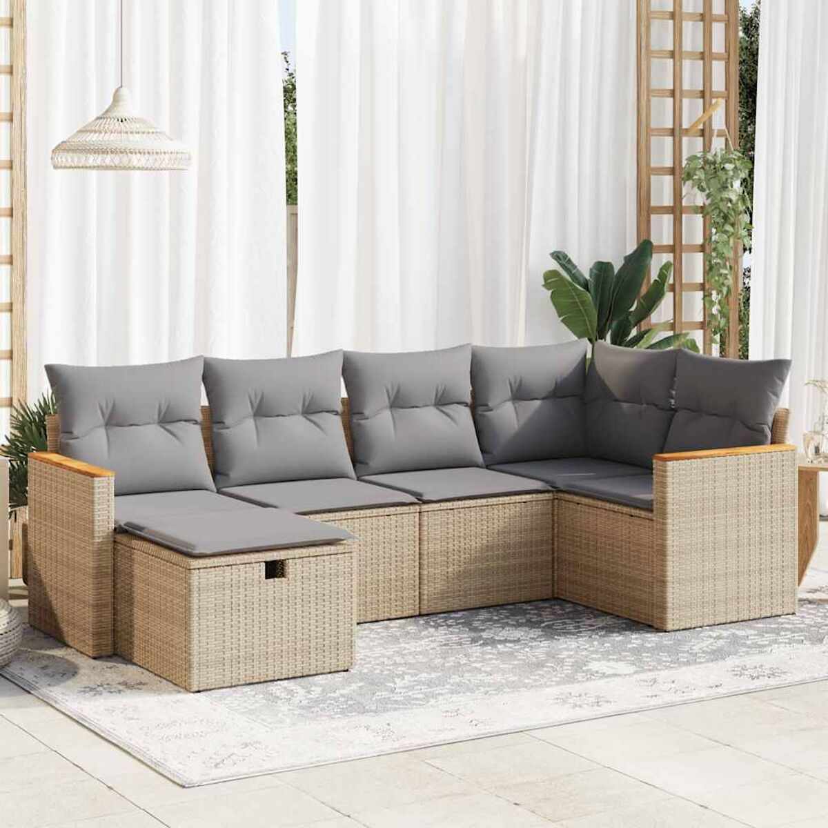 Divano angolare in rattan beige con cuscini grigi su un tappeto, vicino a tende bianche.