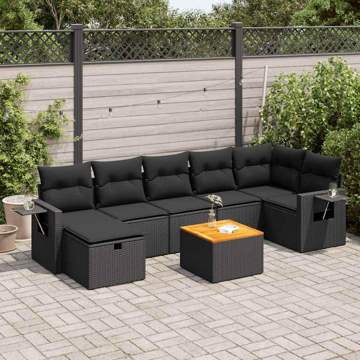 Schwarzes Outdoor-Ecksofa. Schwarze Kissen und Rahmen. Couchtisch davor. Ziegel und Grün.
