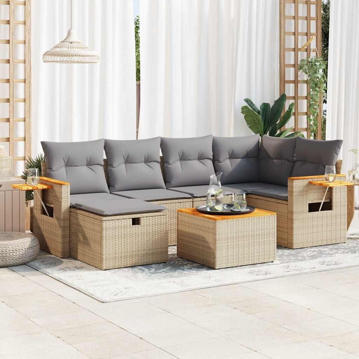Divano componibile in rattan con cuscini grigi, tavolini in legno e tappeto chiaro su un patio.